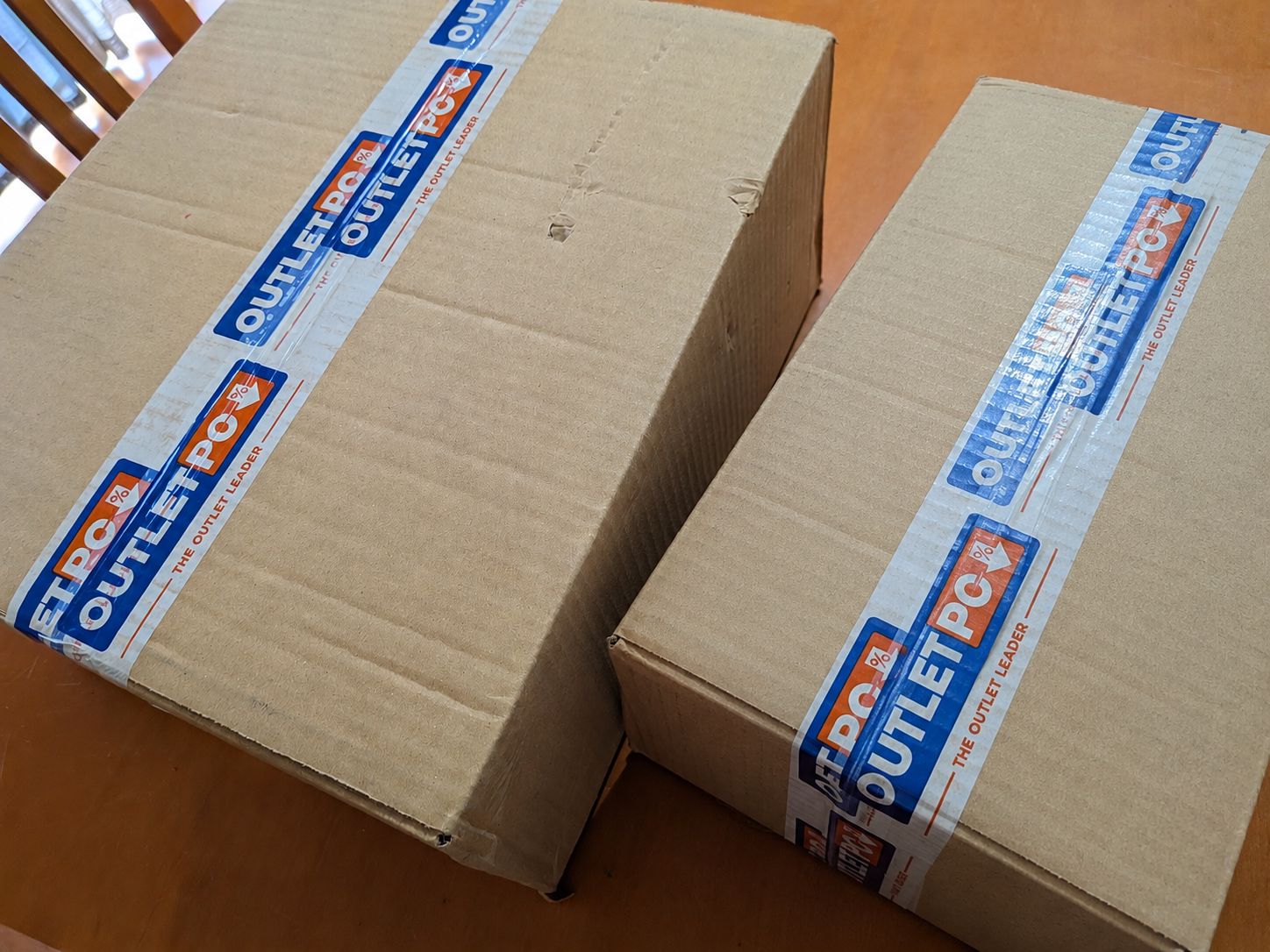 Duas caixas de cartão da Outlet-PC fechadas sobre uma mesa.